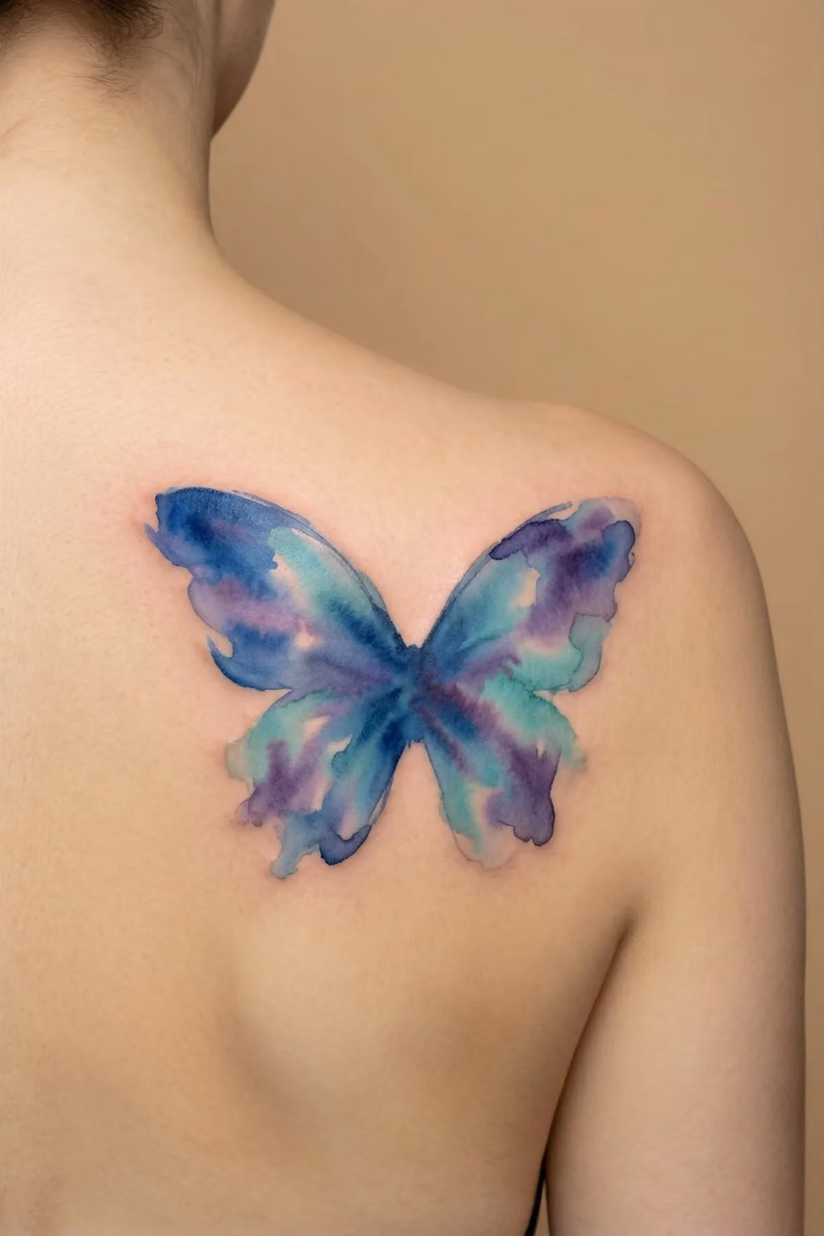 Aquarell-Schmetterling in Blau, Violett und Türkis ohne Konturlinien auf einem Schulterblatt