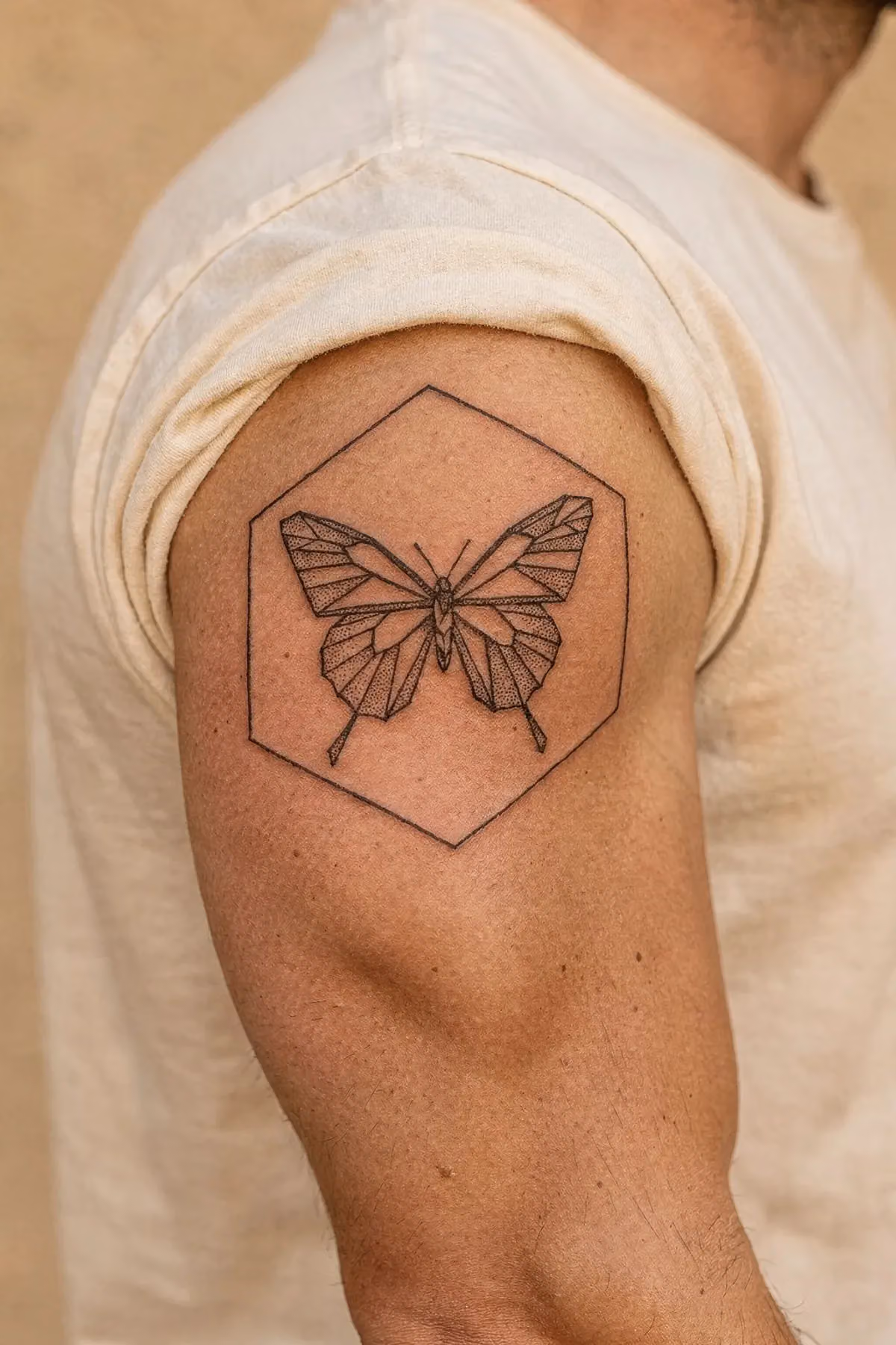 Geometrischer Falter mit Dotwork-Schattierung in einem feinen Sechseck auf dem Oberarm eines Mannes