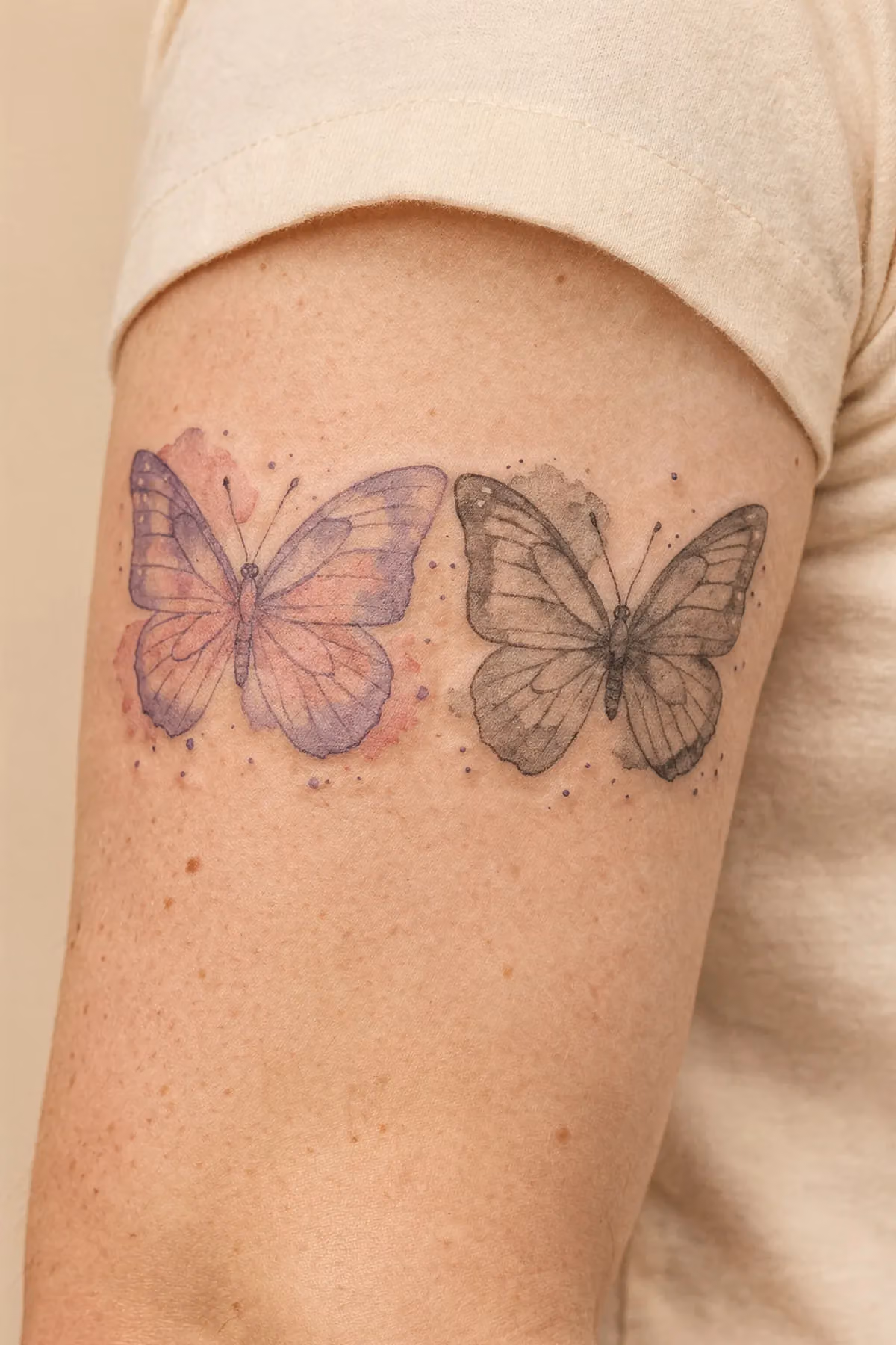 Schmetterlings-Tattoo oberer Arm, Pastelllavendel bis Rosa, Aquarellsprenkel, Graustufen‑Mockup daneben