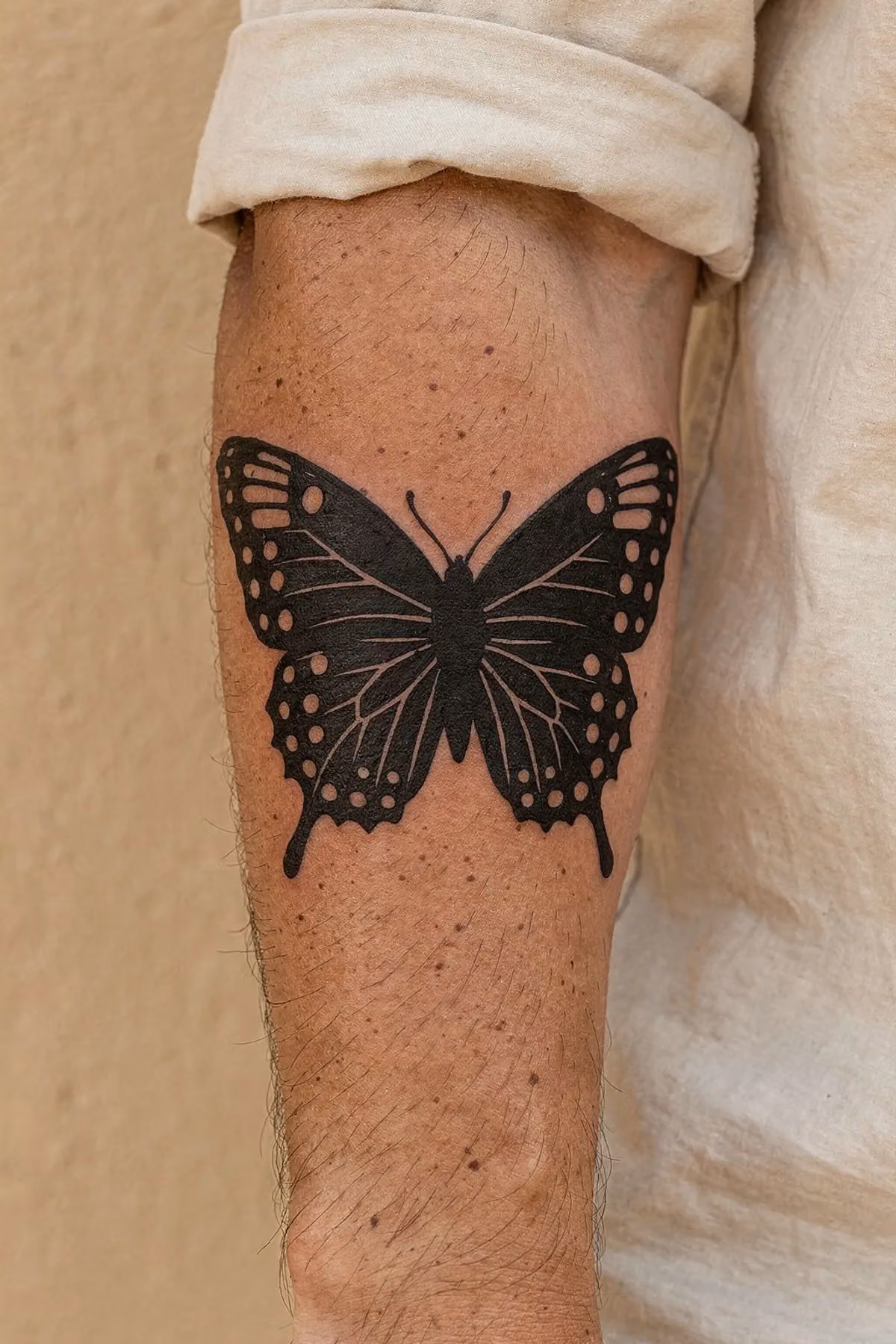 Symmetrischer Blackwork-Falter mit ausgesparten Punkten an der Unterarminnenseite eines Mannes, leicht um den Arm gelegt