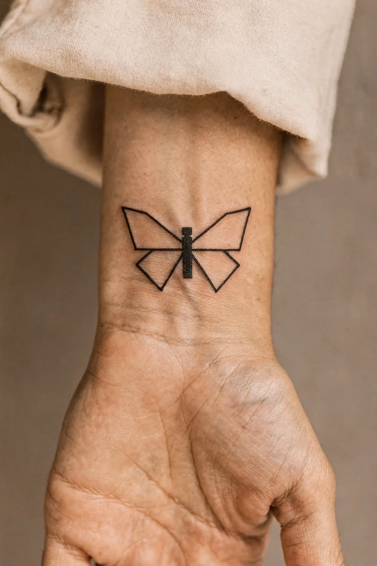 Ein minimalistischer Schmetterling aus Rechteck und Trapezen auf dem Handgelenk, in einfachen schwarzen Linien.