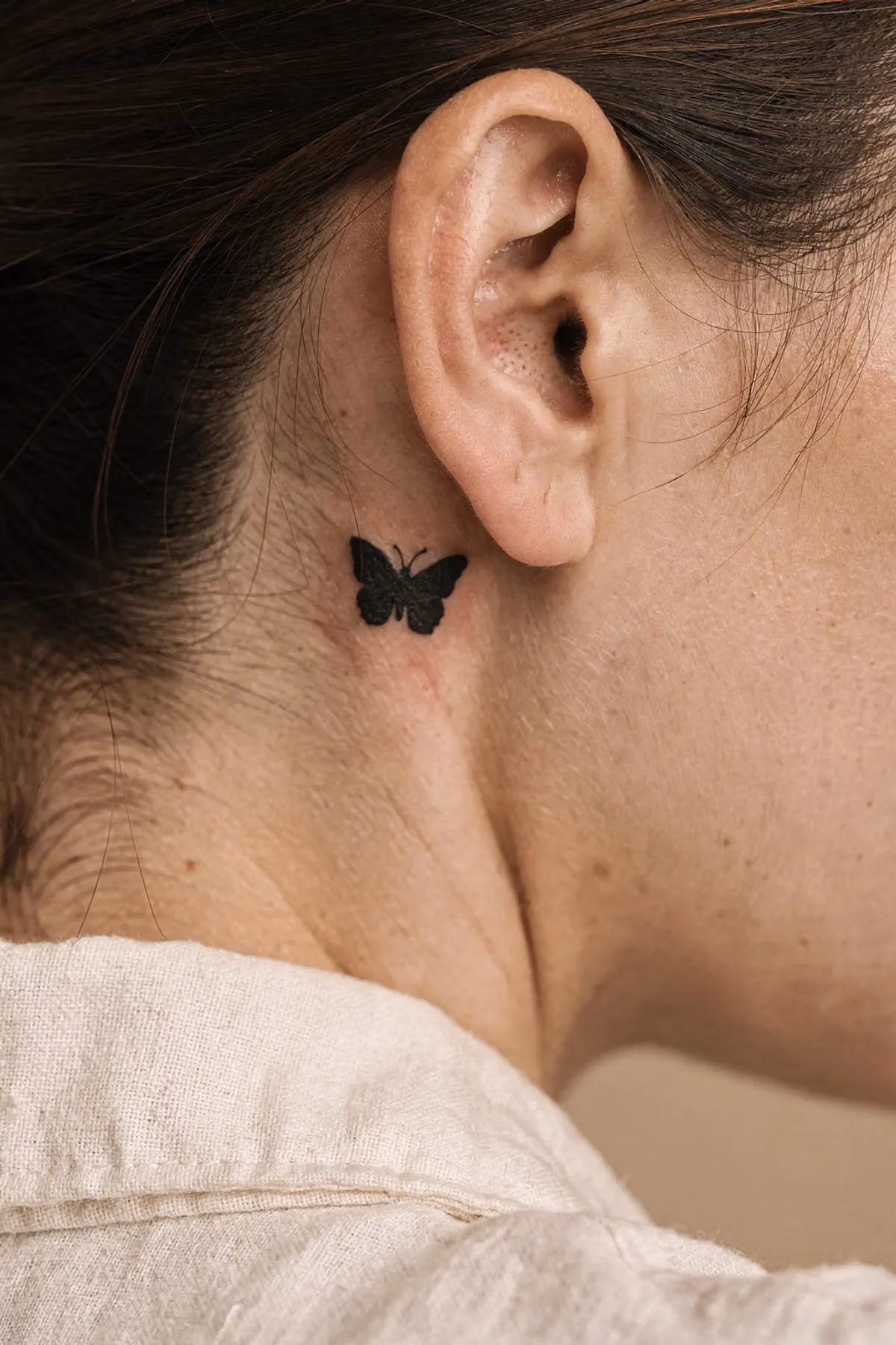 Kleines Silhouette-Schmetterlingstattoo hinter dem oberen Ohransatz, fingergroß, von hinten oben gesehen