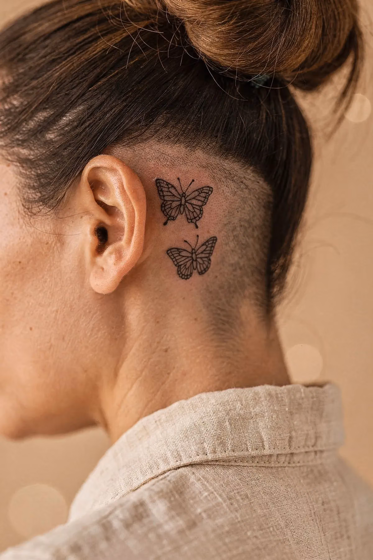Zwei winzige Schmetterling-Tattoos auf der flachen Haut hinter dem Ohr, das Ohr selbst bleibt frei.