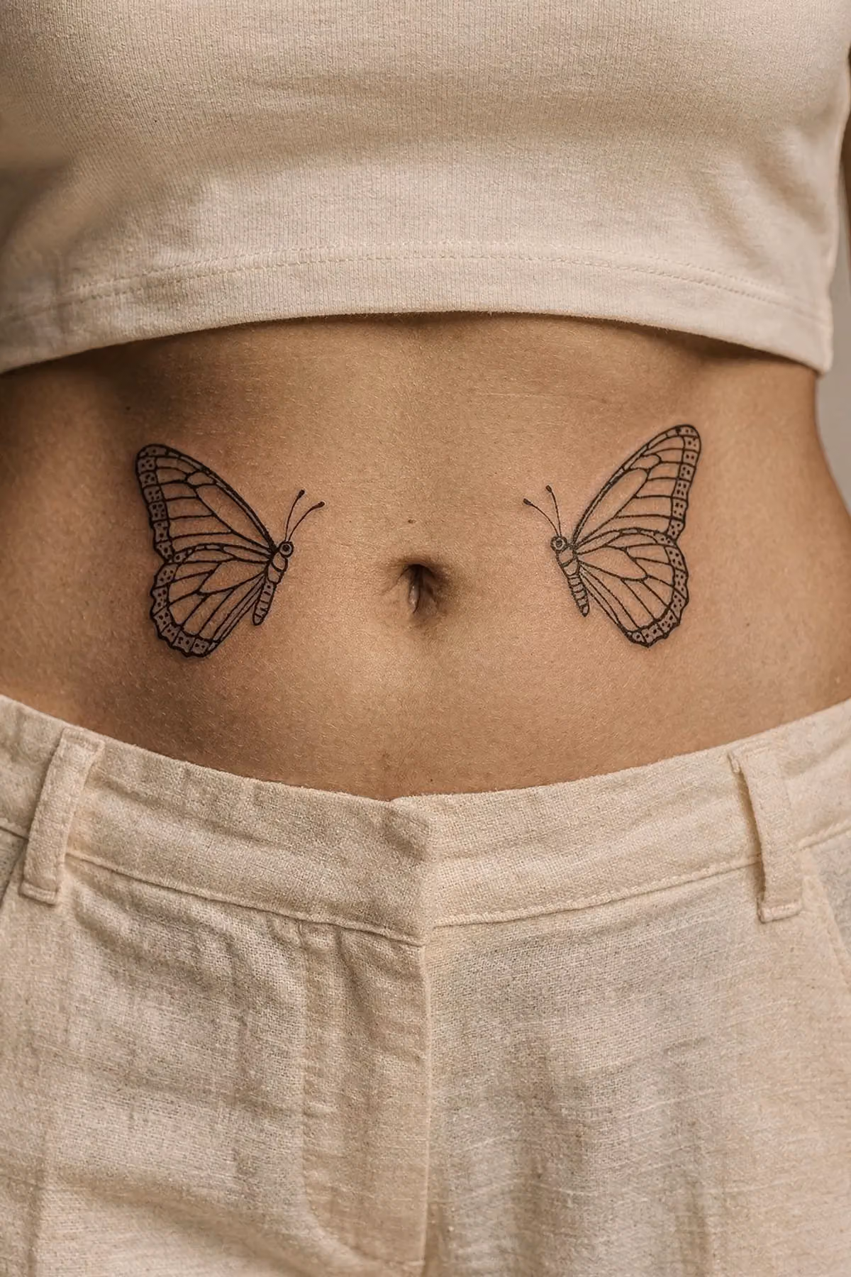 Zwei feine schwarze Schmetterling-Tattoos symmetrisch links und rechts des Bauchnabels.