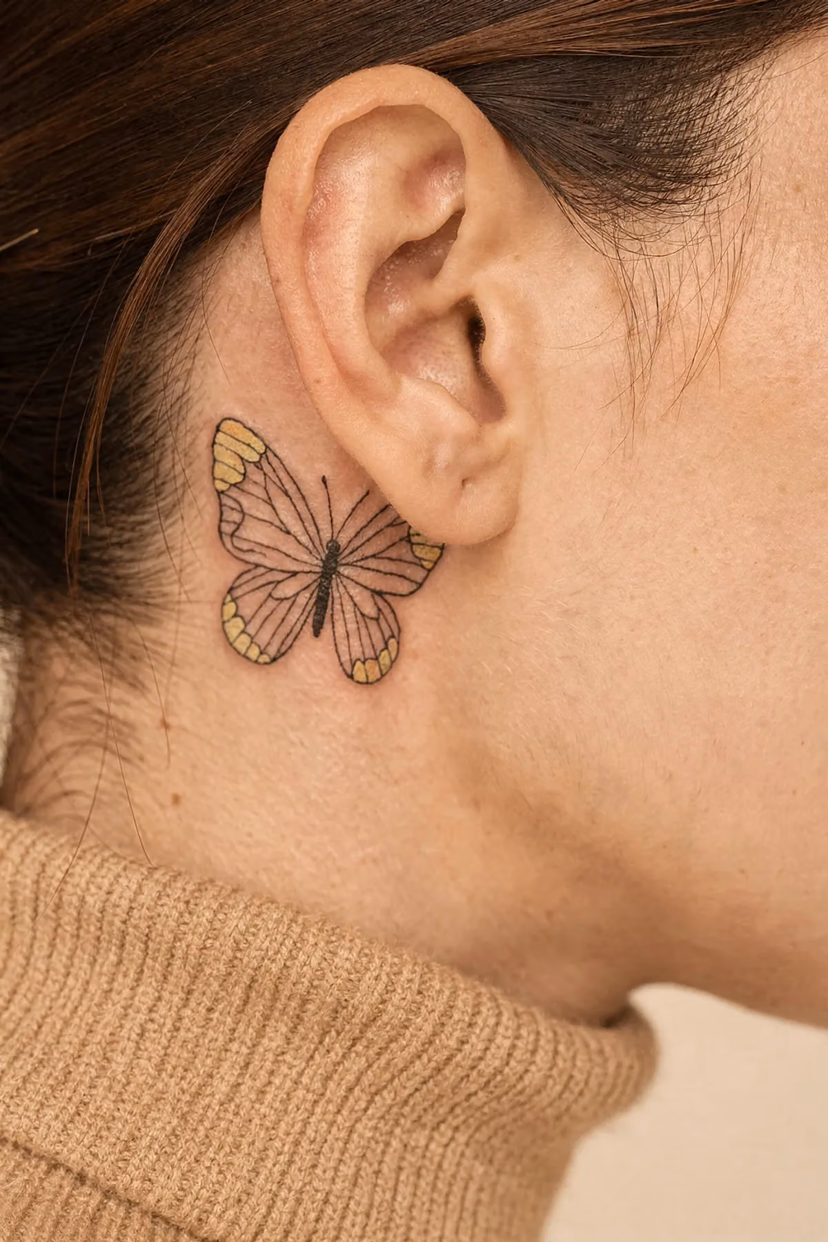 Feinlinien-Schmetterling mit dezenten pastellgelben Flügelakzenten hinter dem Ohr, zwei Fingern breit