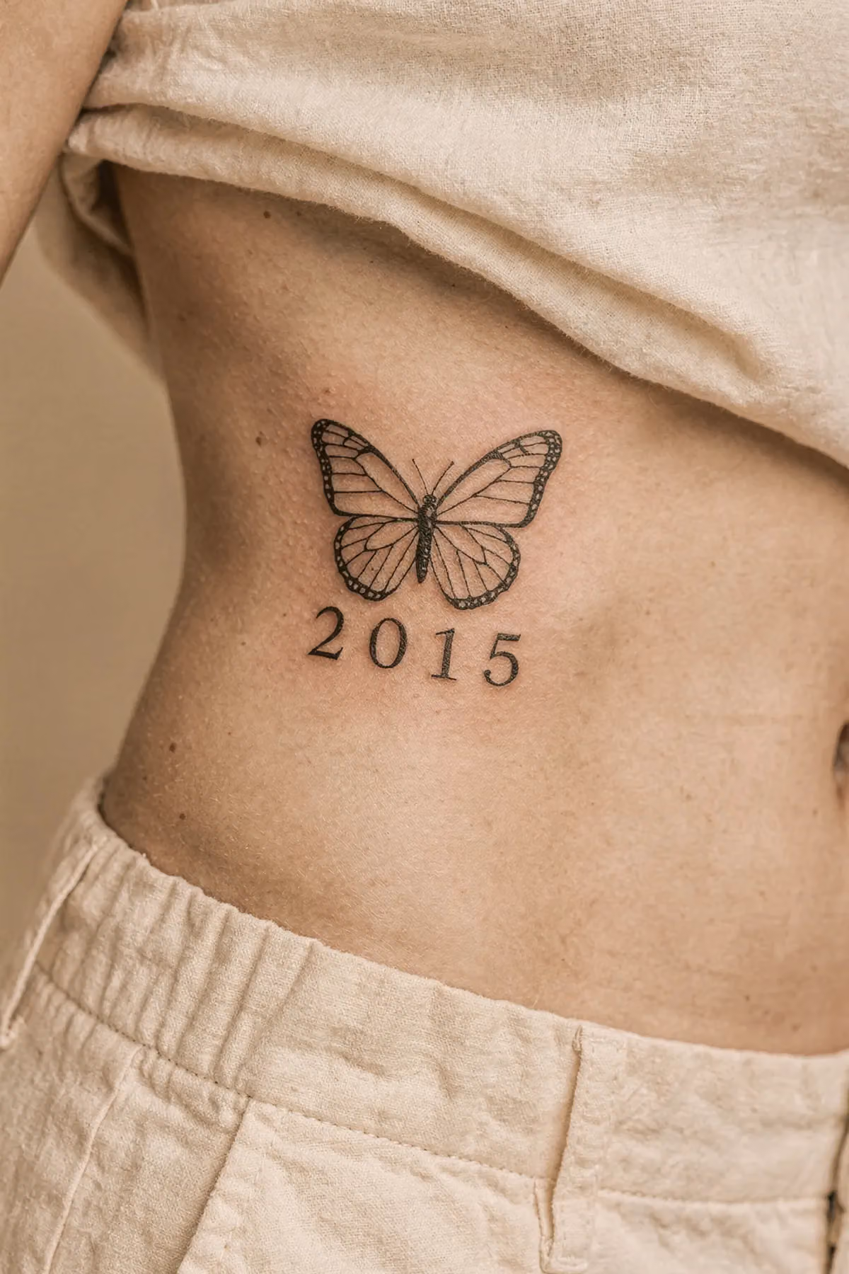 Feinlinien‑Schmetterling über der linken Rippenpartie mit der Jahreszahl 2015 darunter