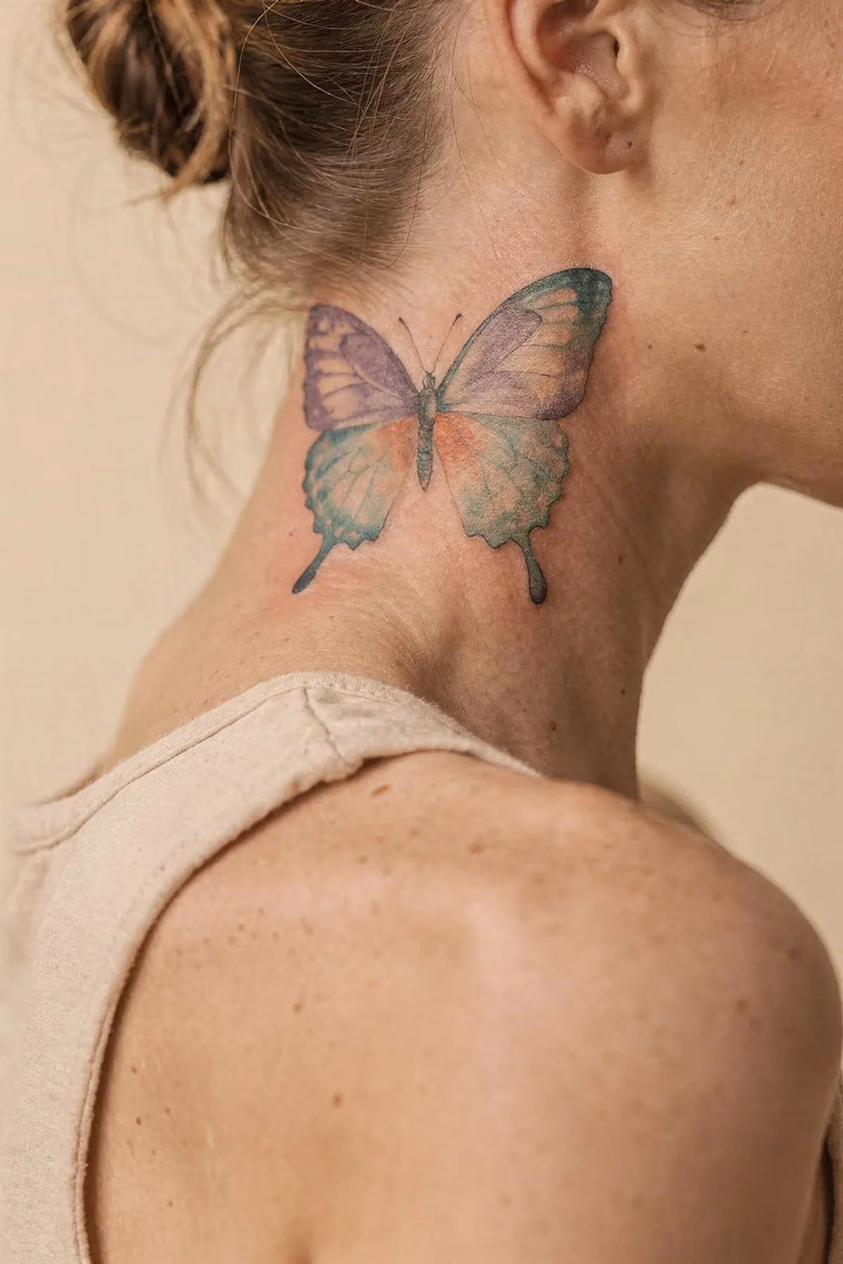 Aquarell-Schmetterling an der Halsseite, Farben Lavendel, Türkis, Koralle verlaufen fließend zur Schulter.