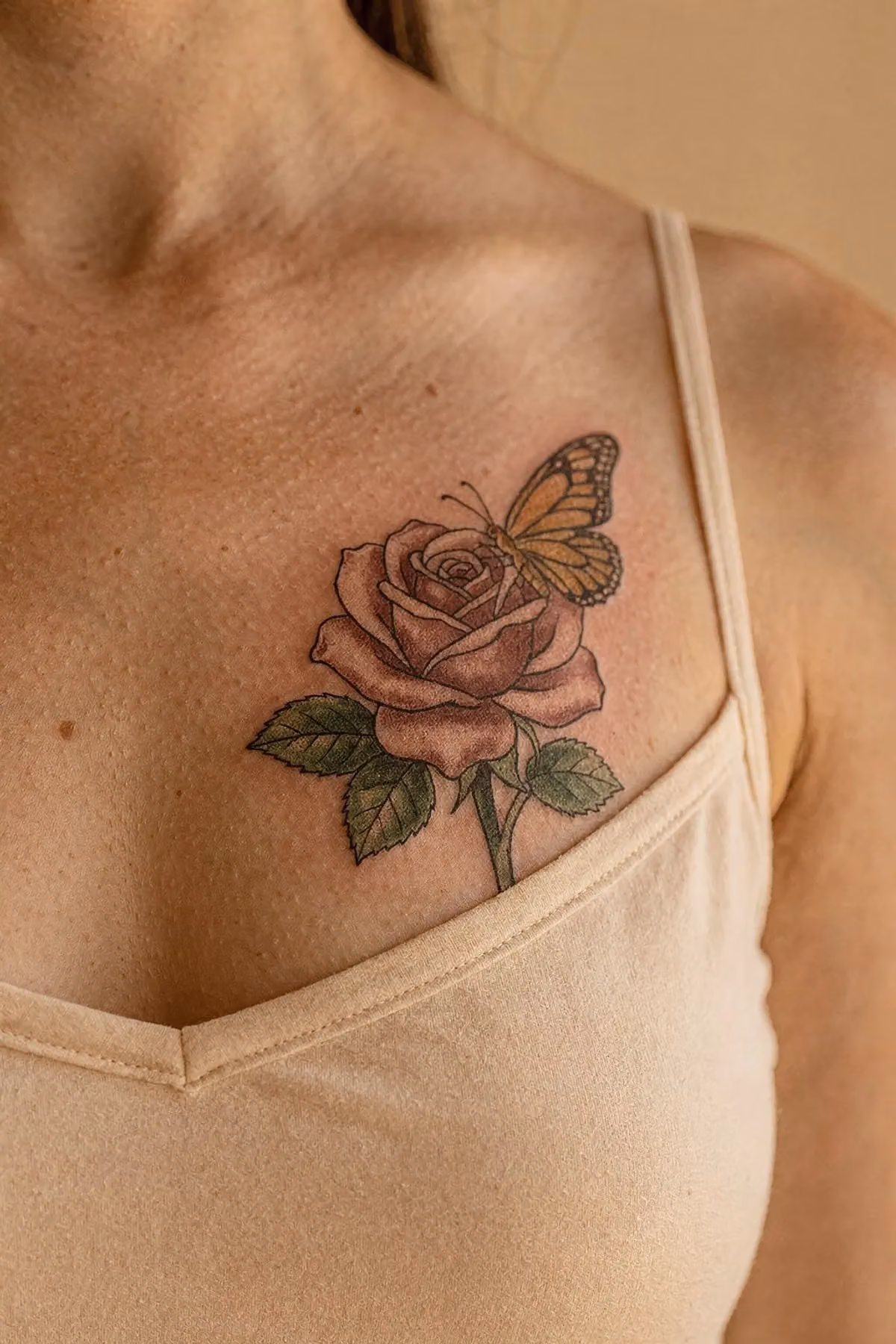 Rose und Schmetterling Tattoo unter dem Schlüsselbein, Rose in gedecktem Altrosa, Falter in Bernstein