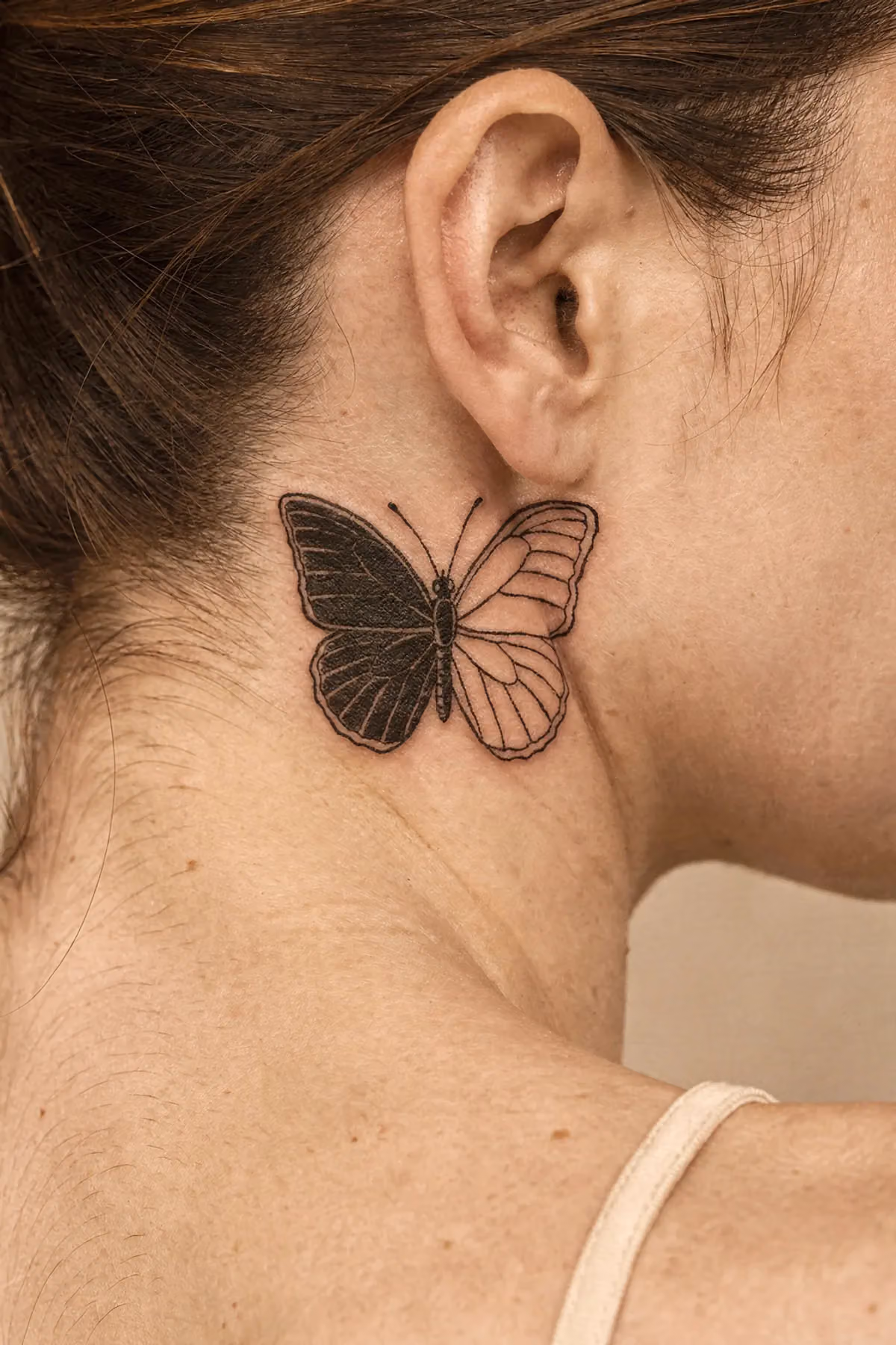 Verheiltes Grafik‑Schmetterlingstattoo mit einem schwarzen und einem umrandeten Flügel hinterm Ohr