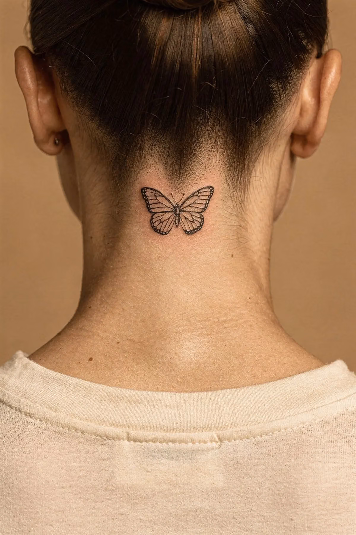 Kleiner Fineline-Schmetterling direkt unterhalb des Haaransatzes im Nacken, Haare hochgesteckt.