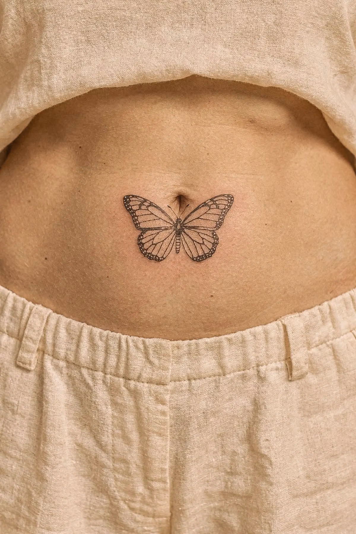 Kleiner Fineline-Schmetterling mittig auf dem Bauchnabel, die Flügel liegen links und rechts davon.