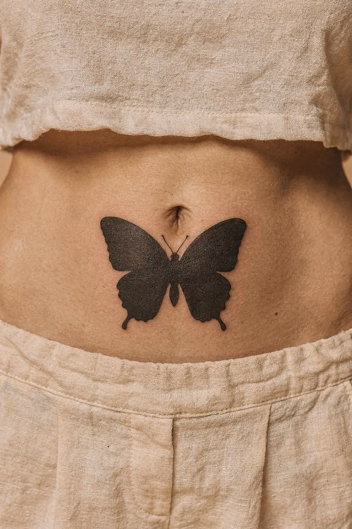 Schmetterling als geschlossene schwarze Silhouette ohne Innenzeichnung, mittig auf dem Bauchnabel.