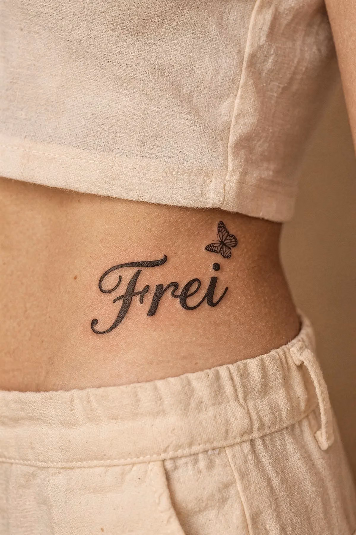 Schriftzug „Frei“ an der Taille, der Punkt über dem i ist ein winziger Schmetterling.
