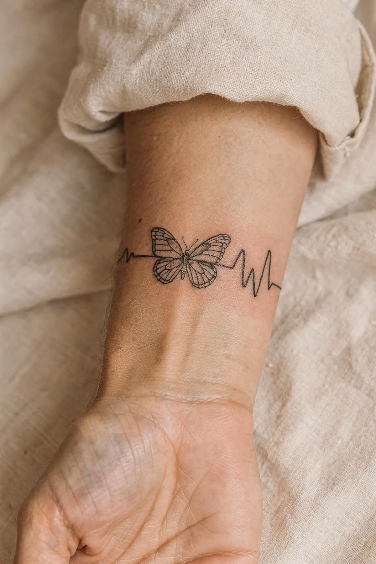 Kleiner Schmetterling am Unterarm, durch den eine haarfeine Pulslinie waagerecht hindurchläuft.