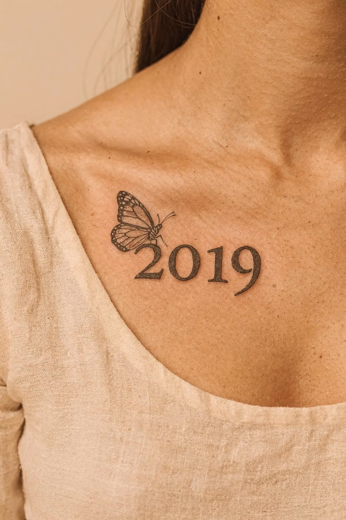 Jahreszahl entlang des Schlüsselbeins, daneben ein kleiner Schmetterling.