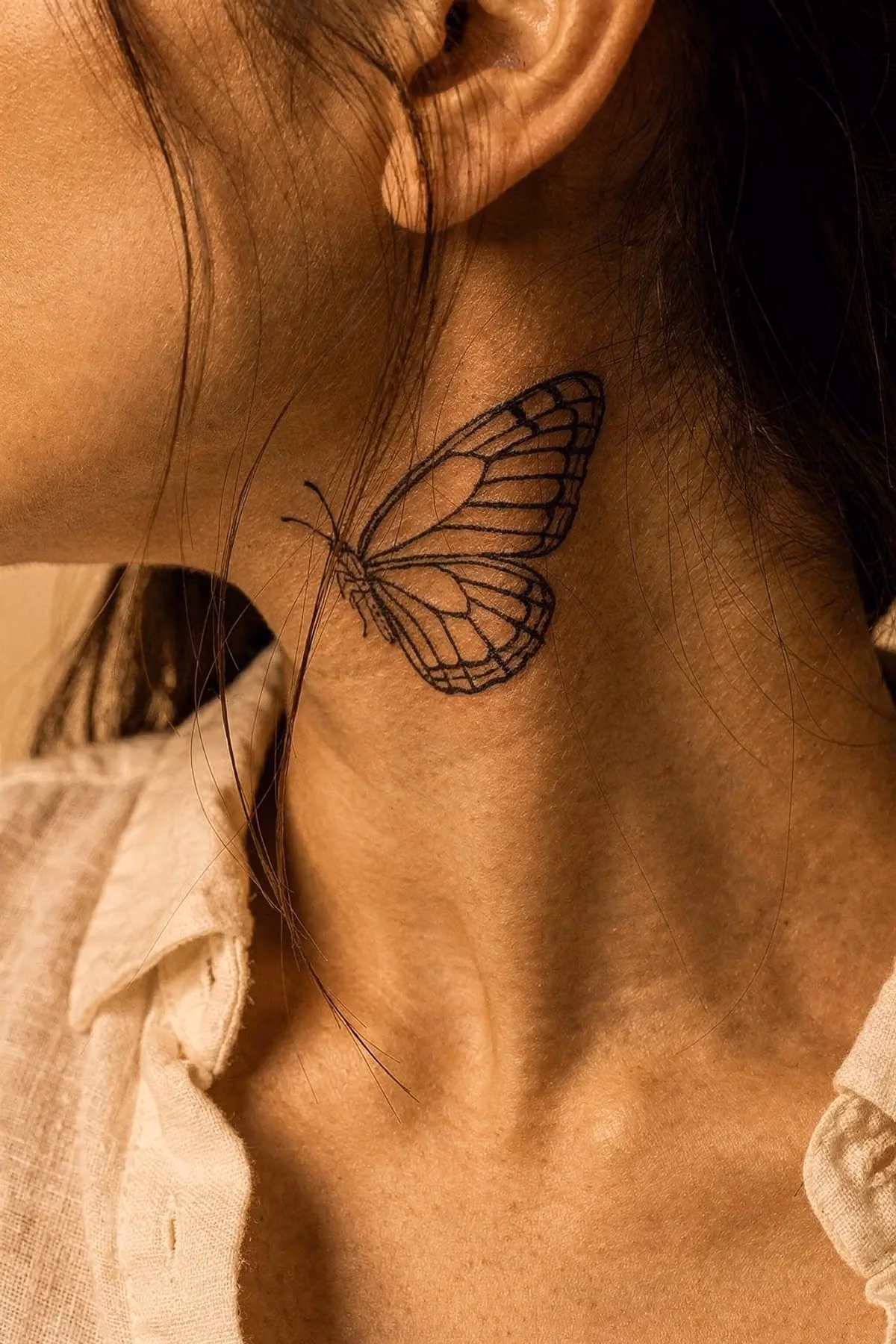 Fineline-Schmetterling seitlich am Hals, zur Hälfte von offen fallendem Haar verdeckt.