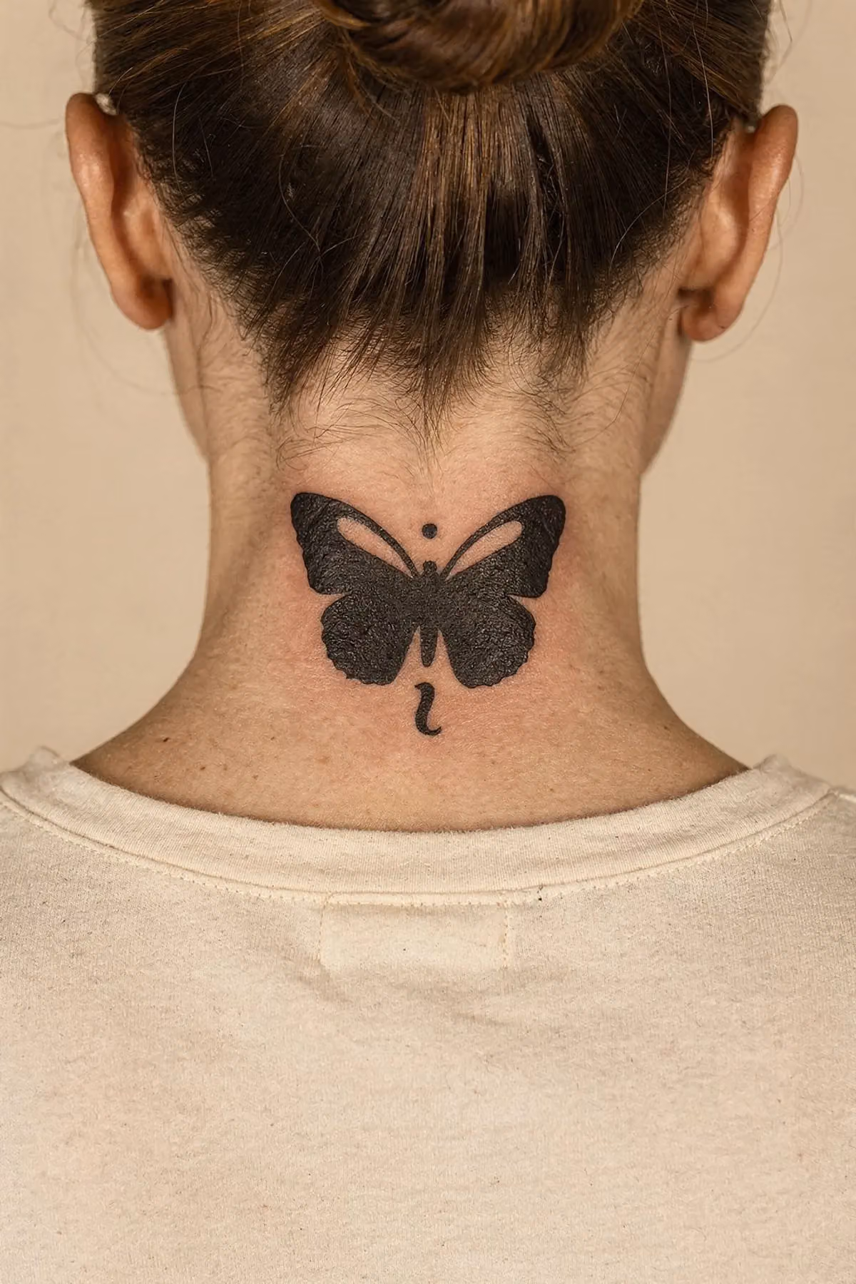 Kräftig schwarz ausgefüllter Schmetterling im Nacken, Punkt über dem Körper, Komma darunter.