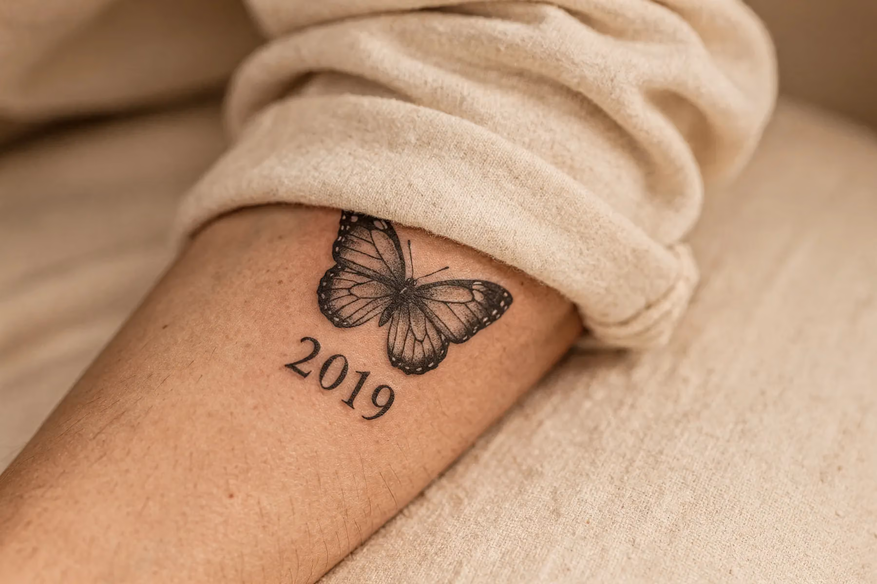 Kleiner schwarz‑grauer Schmetterling am Unterarm, darunter die Jahreszahl 2019 in klarer Serifenschrift