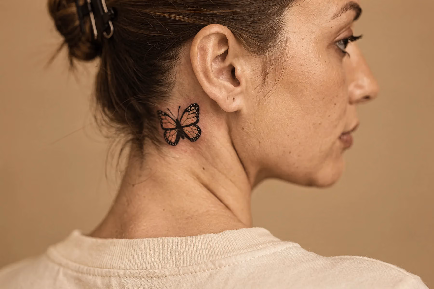 Nahaufnahme: kleines Schmetterling‑Tattoo direkt hinter dem Ohr, Haare locker darüber
