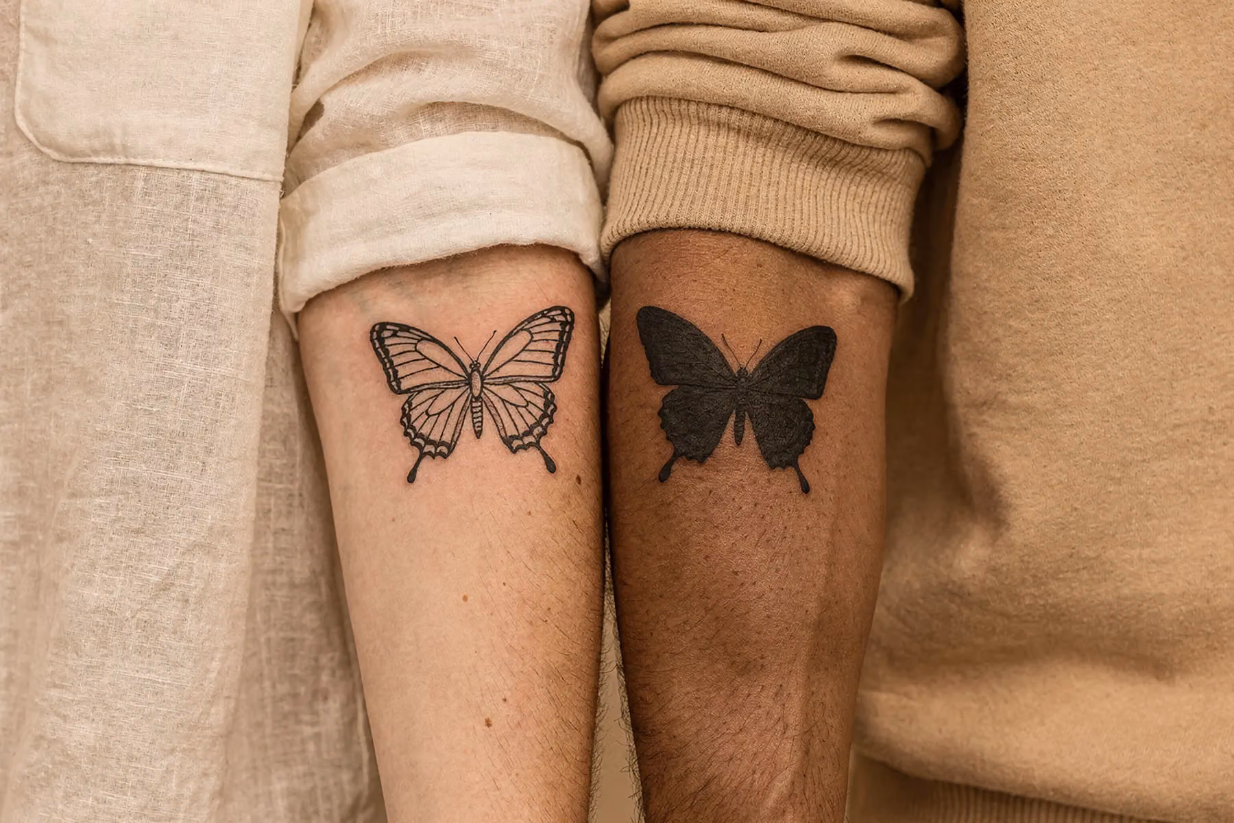 Zwei Hände, die sich leicht berühren, auf jeder Hand ein filigranes Schmetterling Tattoo, wobei die Flügel sich visuell ergänzen und eine Einheit bilden.