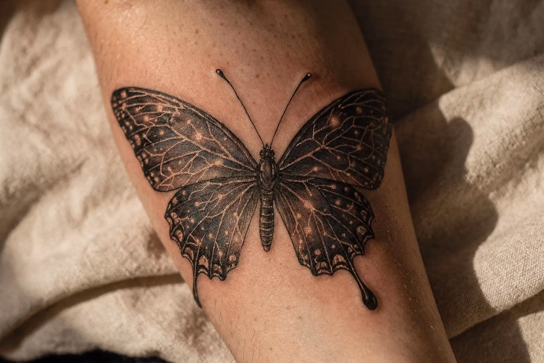 Nahaufnahme eines Schmetterling-Tattoos auf einem Unterarm, dessen Flügelschuppen als filigrane neuronale Netzwerkmuster gezeichnet sind, weich ausgeleuchtet vor cremefarbenem Hintergrund, das die Psyche als zartes, vernetztes Gebilde zeigt.