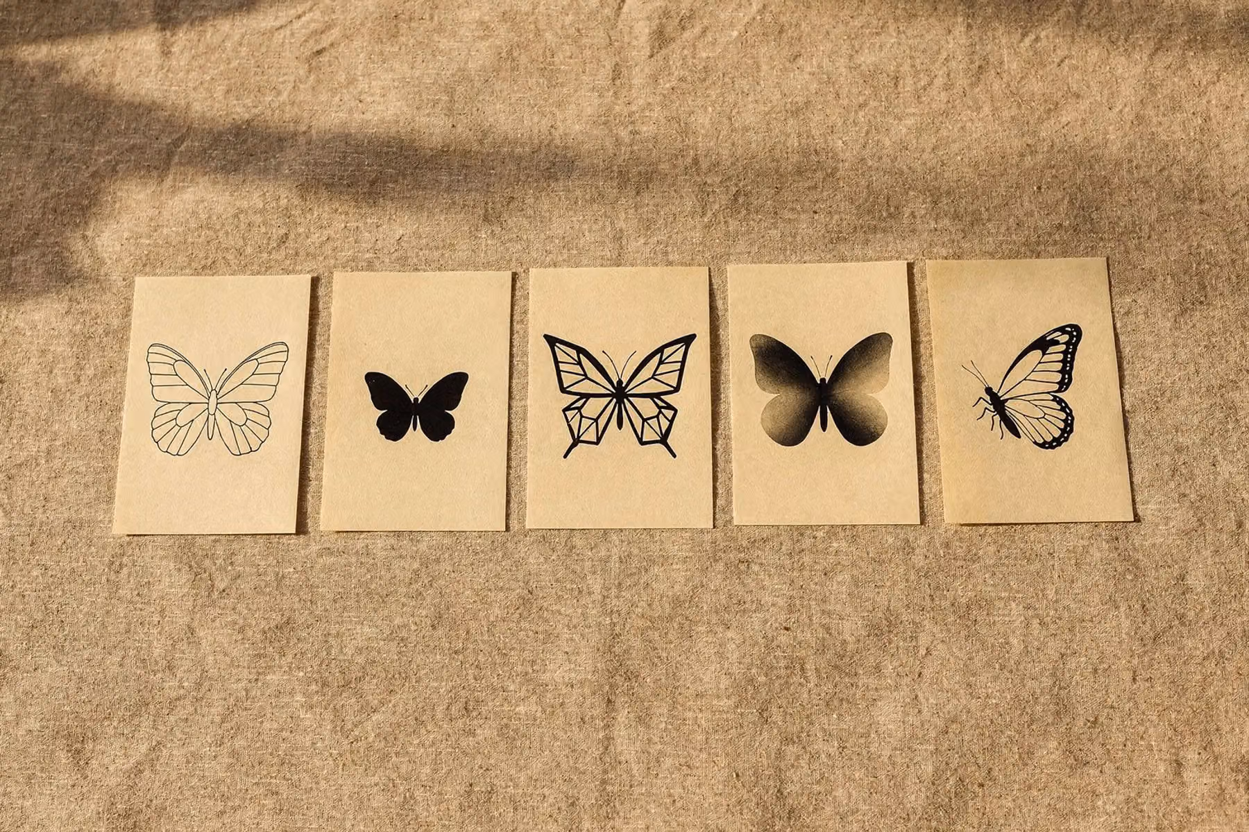 Fünf ausgedruckte Schmetterling Tattoo Vorlagen in einer Reihe auf Leinen: Umriss, Silhouette, Geometrie, Schattierung und Profil