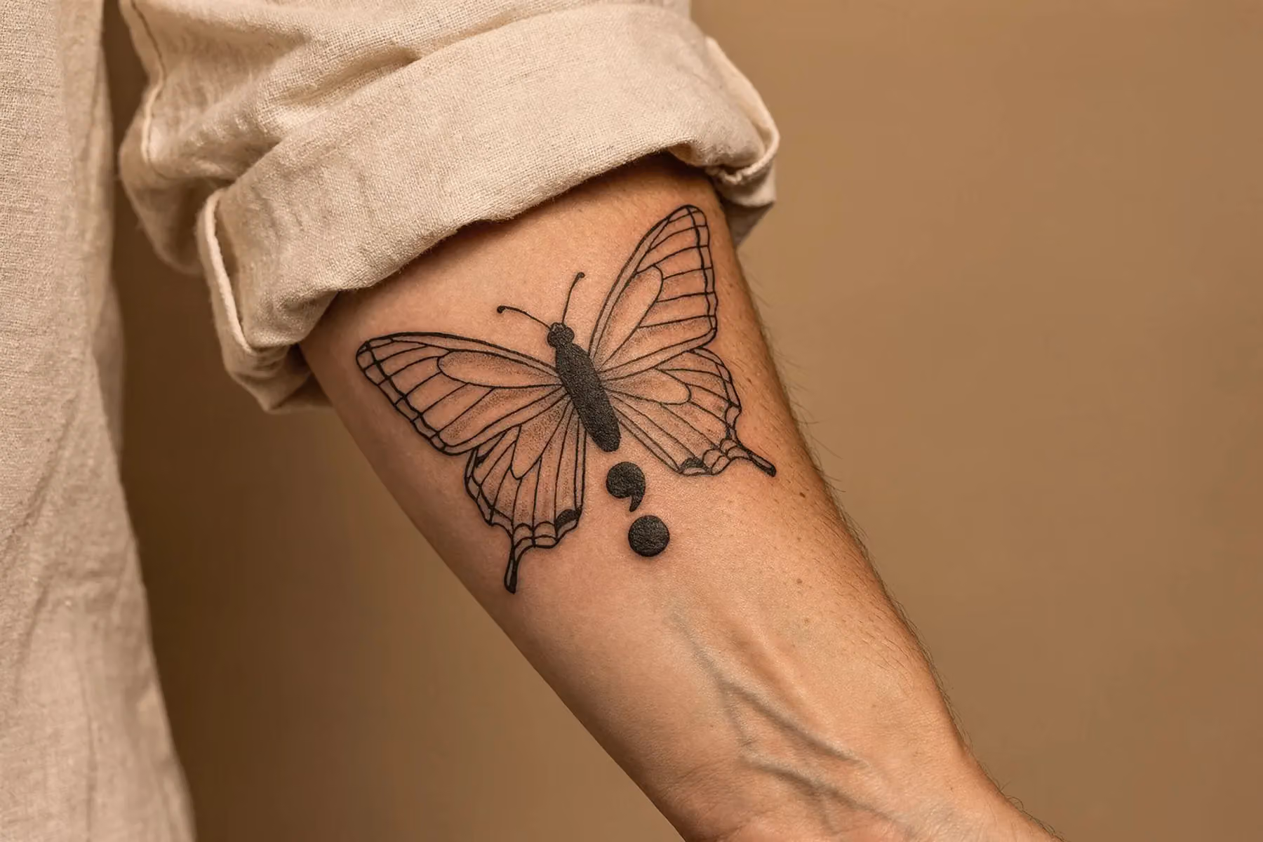 Nahaufnahme eines Schmetterling-Tattoos, bei dem ein schwarzes Semikolon den filigranen Körper bildet, auf cremefarbenem Untergrund mit weichem Seitenlicht.